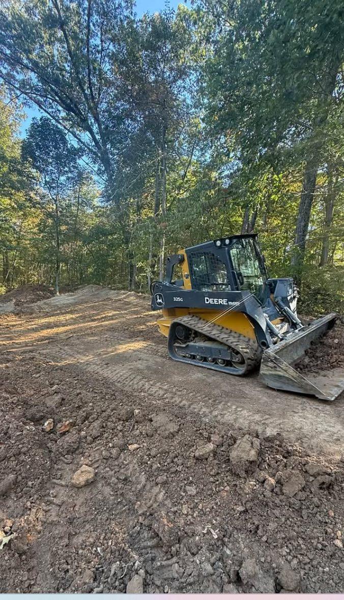 John Deere compact track loader grading a dirt drive through the woods