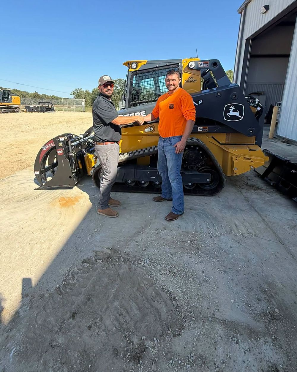 Handshake in front of a new John Deere 331P compact track loader with a grapple bucket